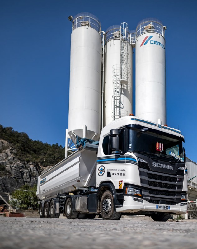 Photo d'ATIL : un camion semi-benne aux couleurs d'ATIL devant des silos de cimenterie